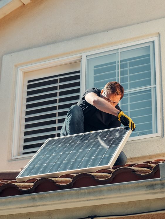 Hombre instalando un panel solar en el techo de una vivienda residencial.