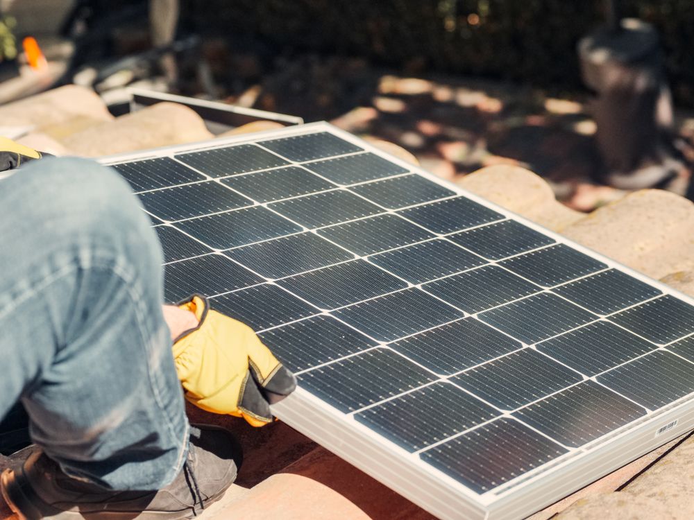 Técnico en equipo de protección instalando paneles solares bajo la luz del sol.